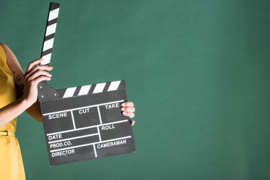 cropped view of woman holding film clapperboard isolated on green with copy space clipart