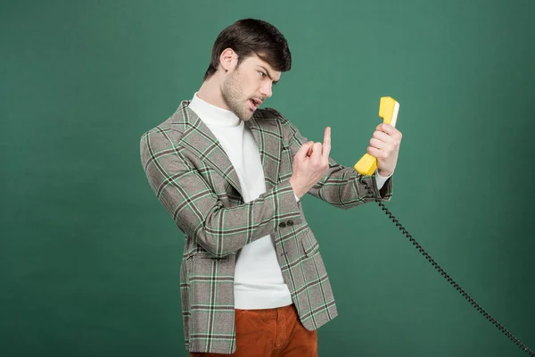 グリーンに分離されたレトロな電話の前で中指を示すのビンテージの服に怒っているハンサムな男 — ストック写真