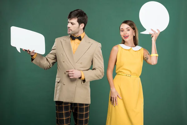beautiful couple in vintage clothes holding speech bubble and thought bubble isolated on green