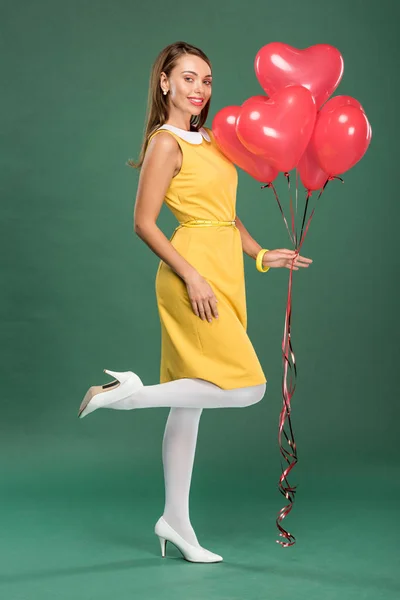 美丽的女人拿着心形气球 看着相机在绿色的背景 — 图库照片