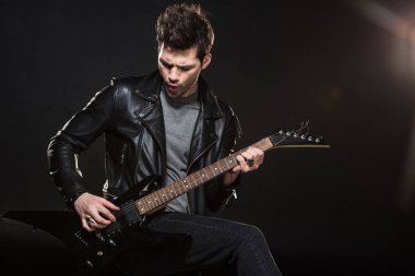 handsome rocker in leather jacket playing electric guitar on black background clipart