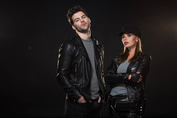 beautiful couple in leather jackets looking at camera and posing on black background