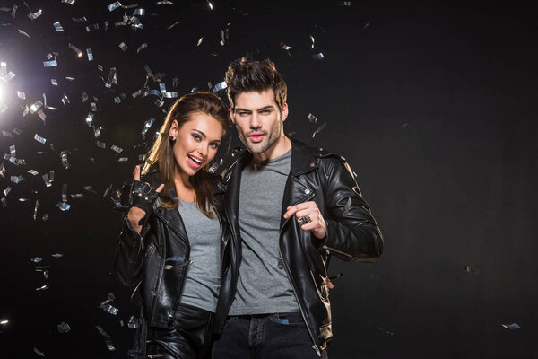 красивая пара в кожаных куртках аплодирует и смотрит в камеру с падающими конфетти на черном фоне
