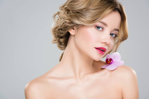 young tender nude woman with purple orchid on shoulder isolated on grey