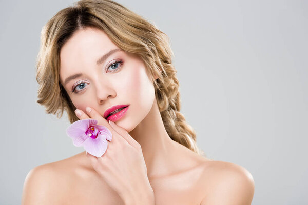 привлекательная девушка держит цветок возле лица изолированы на сером
