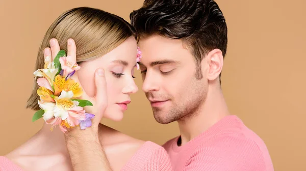 Bonito Namorado Tocando Rosto Namorada Com Flores Rosto Isolado Bege — Fotografia de Stock