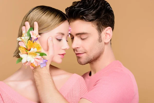 英俊的男人触摸面对的女人与鲜花在脸上孤立在米色 — 图库照片