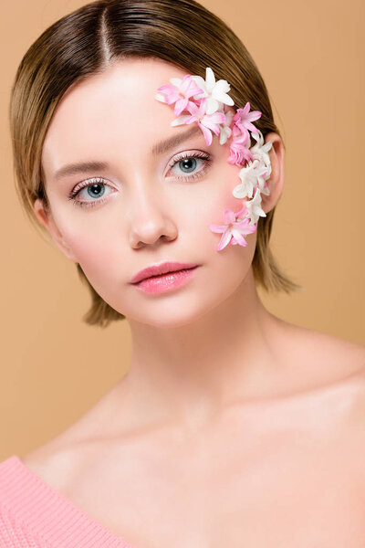 beautiful girl with flowers on face looking at camera isolated on beige