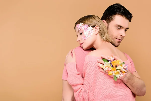 英俊的男人与淡褐色的花朵在手拥抱女朋友与鲜花在米色的脸上 — 图库照片