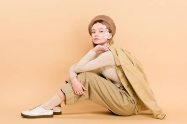 attractive girl in beret posing while sitting on floor isolated on beige  clipart