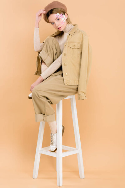 trendy girl in beret sitting on chair isolated on beige 