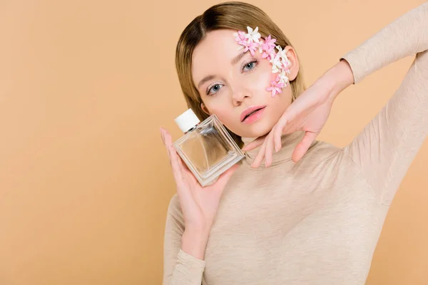 ベージュに分離された香水のボトルとポーズの顔に花を持つ魅力的な女性 — ストック写真