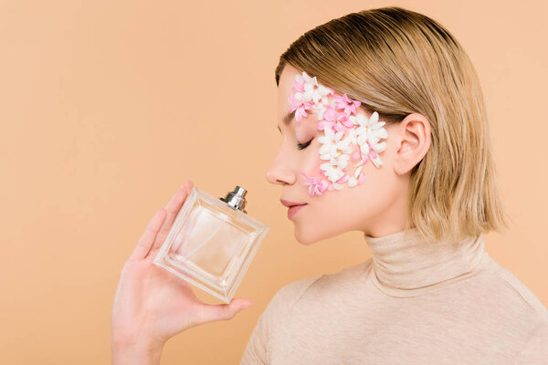 beautiful woman with flowers on face smelling perfume isolated on beige