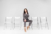attractive woman in formal wear sitting on chair isolated on grey