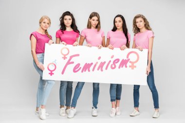 Feminizm yazı ile büyük işareti gri arka plan üzerinde tutan çekici kızlar