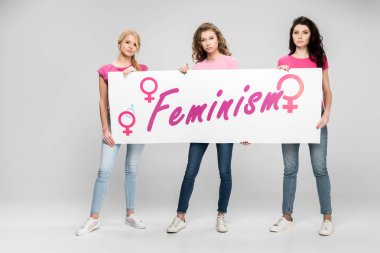 kendine güvenen kızlar büyük işareti feminizm yazı ile gri arka plan üzerinde tutan