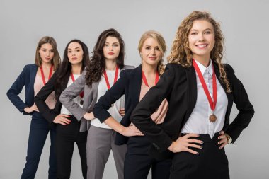 selective focus of cheerful businesswomen standing with medals isolated on grey  clipart