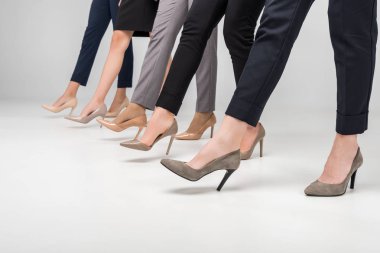 cropped view of businesswomen walking in high heel shoes on grey background clipart