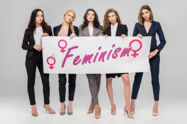 Feminizm yazı ile büyük işareti gri arka plan üzerinde tutan çekici iş kadınları