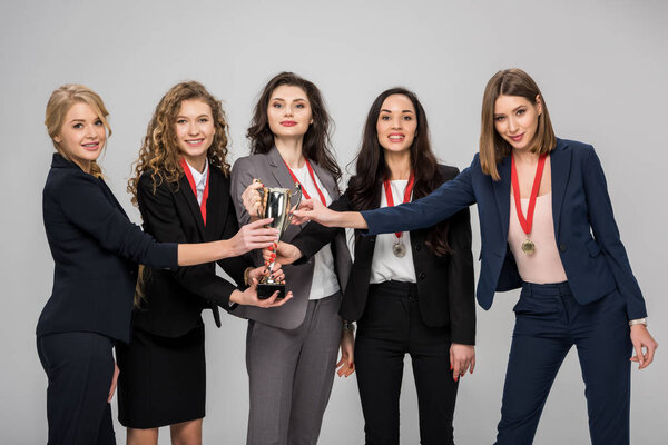successful businesswomen holding trophy smiling isolated on grey 
