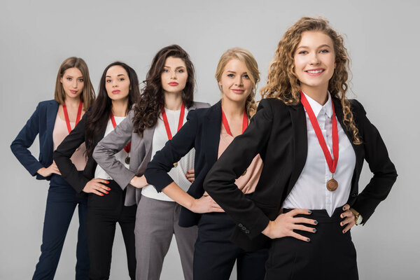 избирательный фокус жизнерадостных деловых женщин, стоящих с медалями, изолированными на сером
 