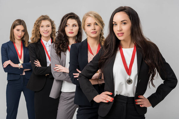 селективный фокус привлекательных молодых бизнесвумен, стоящих с медалями, изолированными на сером
 