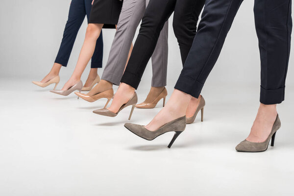 cropped view of businesswomen walking in high heel shoes on grey background
