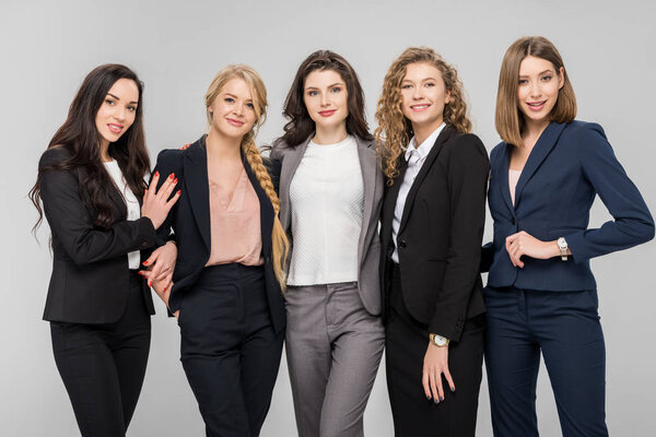 beautiful young businesswomen standing and smiling isolated on grey