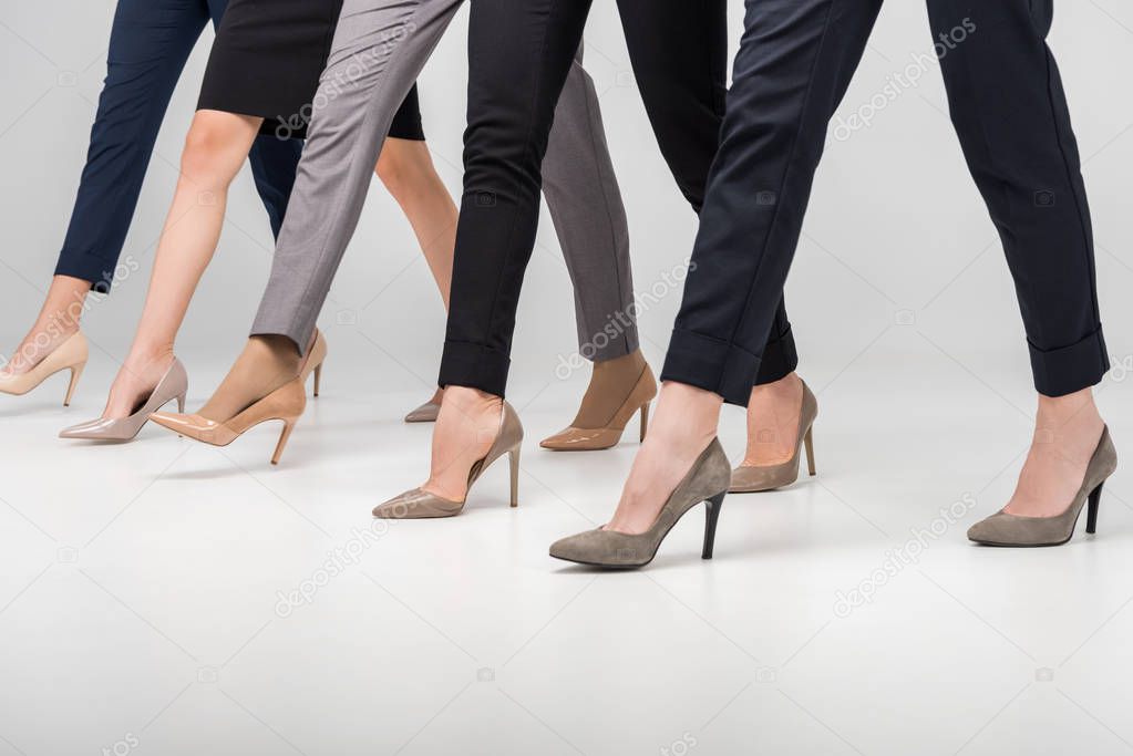 cropped view of women walking in high heel shoes on grey background