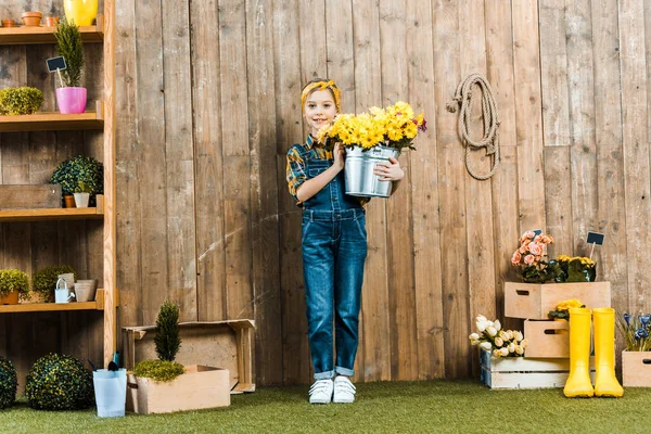 かわいい子供はバケツで花を保持して 木製のフェンスの近くに立って — ストック写真