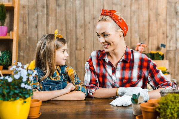 веселая мать смотрит на милую дочь рядом с растениями
 