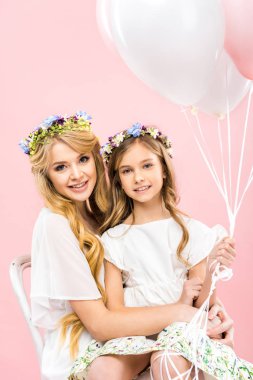 Anneler dizlerinin üstüne oturan ve Festival hava balonları pembe bir arka plan üzerinde tutan çok güzel çocuk