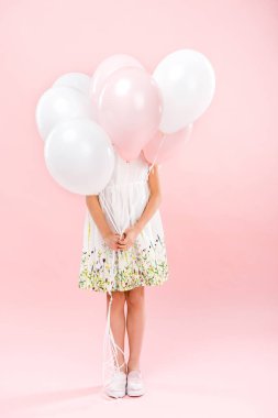 pembe bir arka plan üzerinde beyaz ve pembe hava balonları arkasına saklanmış hassas beyaz elbiseli çocuk