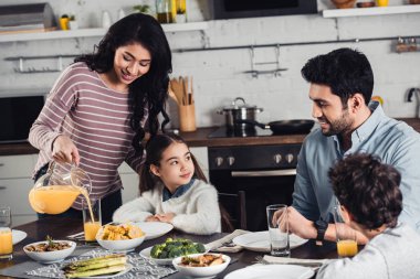 Öğle Yemeği saatinde kızı kocası ve oğlu yakınındaki bardak içine portakal suyu dökülen neşeli latin anne