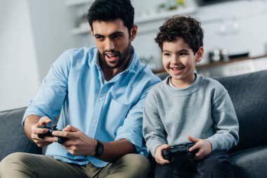 cheerful latin father and son playing video game at home