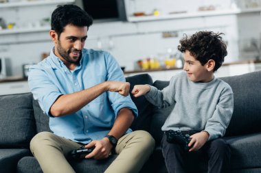 cheerful latin father giving fist bump to son after playing video game at home  clipart