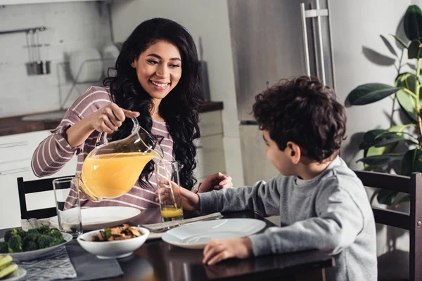 Cheerful Latin Mother Pouring Orange Juice Glass Son Home — Stock Photo, Image