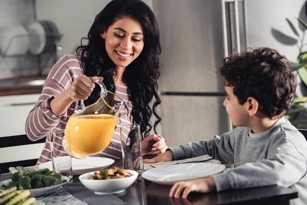 Mãe Latina Feliz Derramando Suco Laranja Vidro Filho Casa — Fotografia de Stock