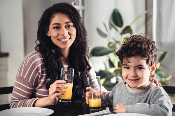 Feliz Madre Latina Lindo Hijo Sosteniendo Vasos Jugo Naranja Cocina — Foto de Stock