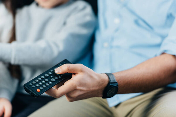 cropped view of man holding remote control in hand near kids