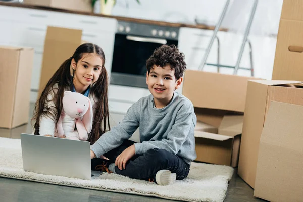 Crianças Felizes Usando Laptop Enquanto Sentado Tapete Nova Casa — Fotografia de Stock