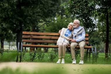 kucaklayan ve Park ahşap bank üzerinde dinlenme sırasında elele üst düzey çift gülümseyen