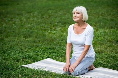 elleriyle diz yoga mat meditasyon poz oturan gülümseyen kadın kıdemli