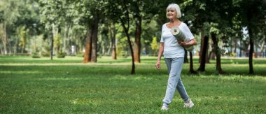 parkta yürüyüş ve fitness mat tutan mutlu kadın kıdemli