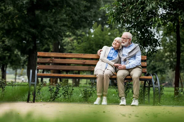 Улыбающаяся Пожилая Пара Обнимается Держится Руки Отдыхая Деревянной Скамейке Парке — стоковое фото