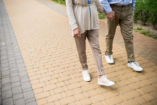 cropped view of senior couple walking across paved sidewalk in park