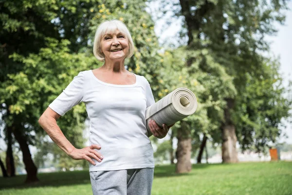 Smiling Senior Woman Holding Yoga Mat While Holding Hand Hip — Stock Photo, Image