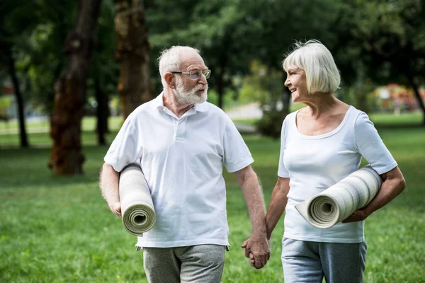 happy senior couple with fitness mats talking while walking in park