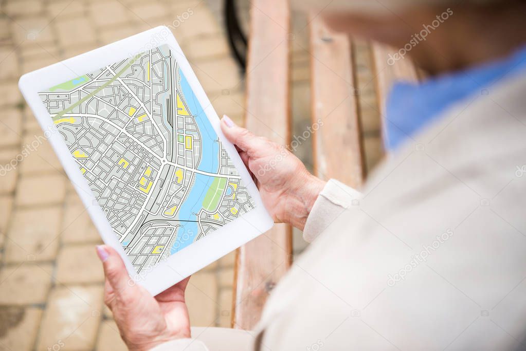 selective focus of senior woman holding digital tablet with map on screen