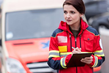 Female paramedic in red uniform writing in clipboard clipart